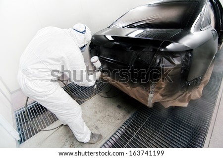 Worker painting a car in garage using an airbrush gun