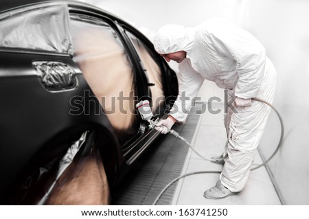 Detail of automotive engineer, mechanic painting a black car in workshop