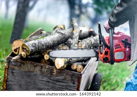 Close up of forest worker, lumberjack with chainsaw against logs and foggy forest background