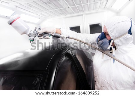 automotive worker painting a black car in a special booth