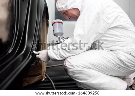 Worker preparing black paint for body work on a car wearing white special suit