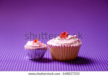 Close-up two, big and small, colorful and natural velvet cupcakes with butter cream topping and cookie on top isolated on purple background