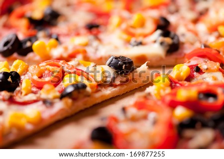 Close-up of slice of dinner pizza with ham, olives, mozzarella, pepperoni and tomatoes