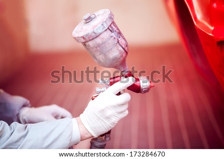 Worker painting a red car in painting booth using professional tools and spray gun Worker painting a red car in painting booth using professional tools and spray gun
