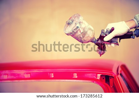 Worker hand painting a red hood of car in auto workshop