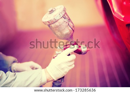 Worker painting a red car in painting booth using professional tools and spray gun