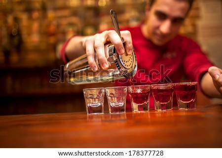 barman with cocktail shaker pouring red alcoholic drink into glasses in bar
