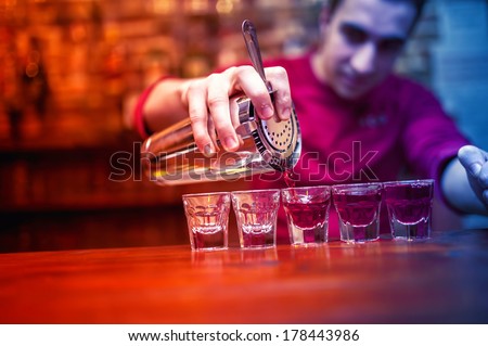 barman with cocktail shaker pouring red alcoholic drink into glasses in bar