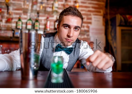 Portrait of barman behind bar with cocktail tools and drinks on bar