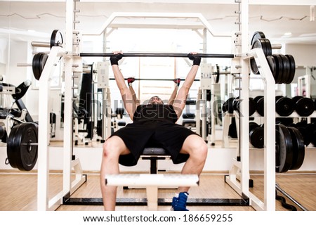 bodybuilder training in the gym: chest - barbell bench press, wide grip
