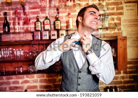Portrait of angry and stressed bartender or barman with bowtie behind the bar with alcoholic drinks around. Stressful lifestyle of barista concept