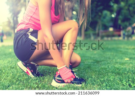 Close-up of active jogging female runner, preparing shoes for training and working out at fitness park