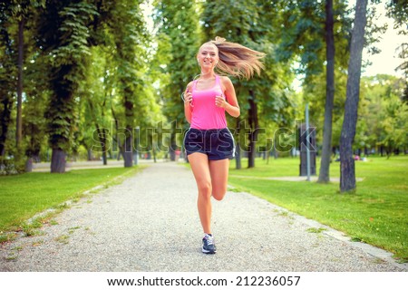 healthy and happy woman running in urban park with headphones and music