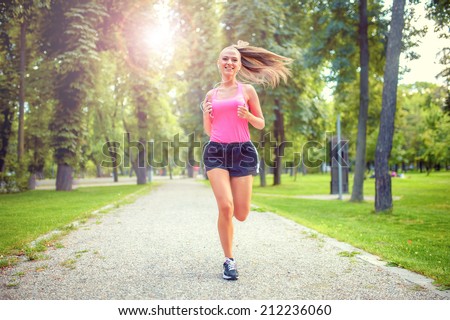 healthy and happy woman running in urban park with headphones and music