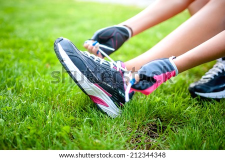Close-up of active jogging female runner, preparing shoes for training and working out at urban fitness park