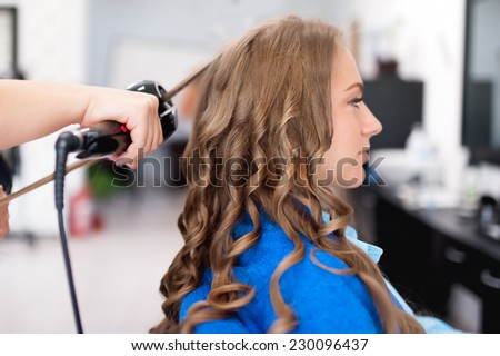 professional hairdresser using curling iron for hair curls at salon