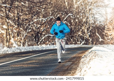 Man fitness concept - running and jogging, outdoor training in snow on a cold sunny day