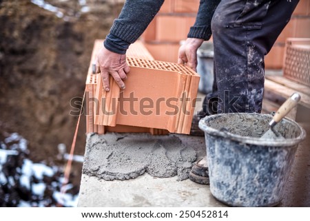 Construction site of new house, worker building the brick wall with trowel, cement and mortar