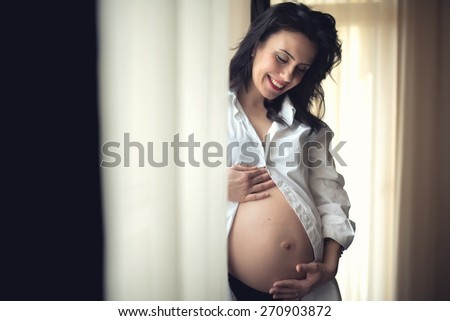 Happy mother holding hands on baby bump, pregnant belly. Cozy portrait of beautiful pregnant woman being happy