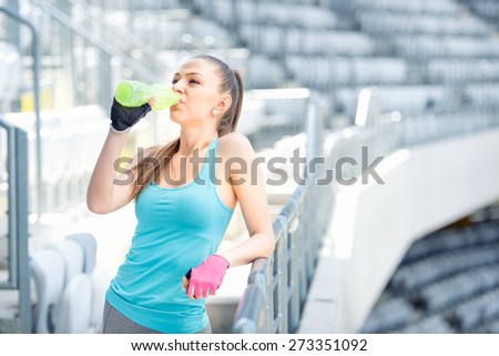Fitness concept - young woman drinking water during workout, training. Cross fit workout on stairs, squats and exercises