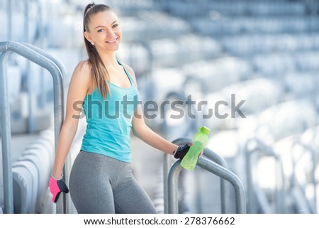 Fitness concept - sexy woman drinking water during workout and training. Cross fit workout on stairs, squats and exercises