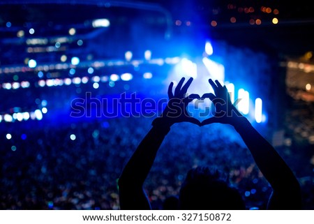 Heart shaped hands at concert, loving the artist and the festival. Music concert with lights and silhouette of a man partying
