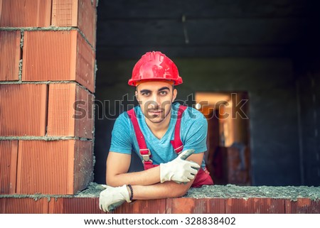 portrait of industrial worker on construction site, sitting and relaxing after a hard day at work. Brick mason worker with protective gear