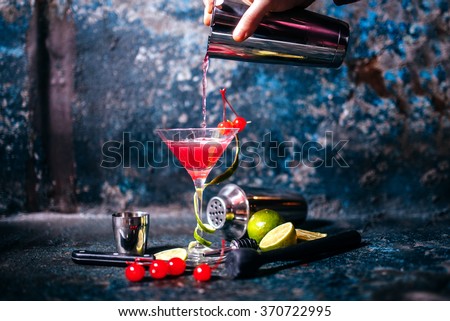 barman preparing and pouring red cocktail in martini class. cosmopolitan cocktail on metal background