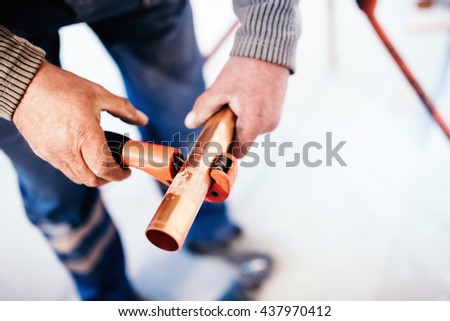Industrial Plumber cutting a copper pipe with a pipe cutter.