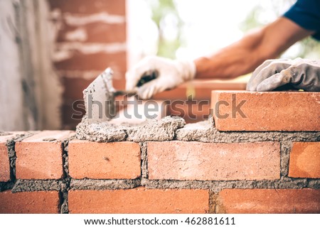 Bricklayer worker installing brick masonry on exterior wall with trowel putty knife