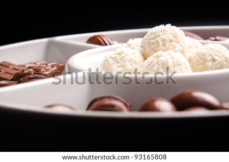 White chocolate balls and brown pieces of chocolate on plate, isolated on black background