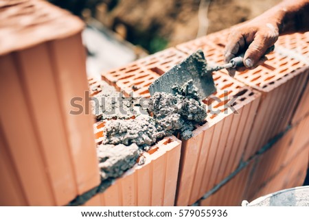Industrial worker using trowel and tools for building exterior walls with bricks and mortar