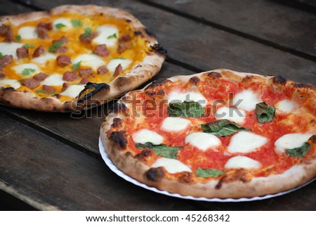 Two freshly-made brick oven pizzas with fresh basil, mozzarella and sausage