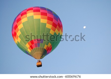 A rainbow colored hot-air balloon in the sky on a beautiful early summer morning. Moon in the distance.