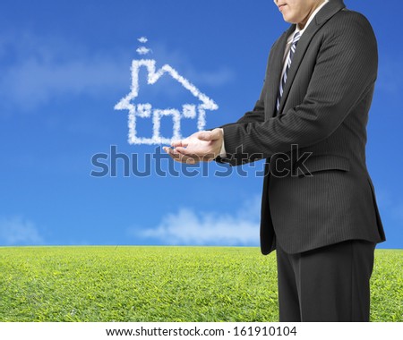 Palm opening businessman with cloud shape house in green meadow and blue sky background