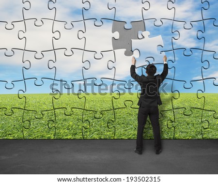 Businessman assembling last missing puzzle on wall for landscape