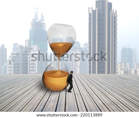 businessman hold the inclined hourglass on wooden floor with city skyscraper