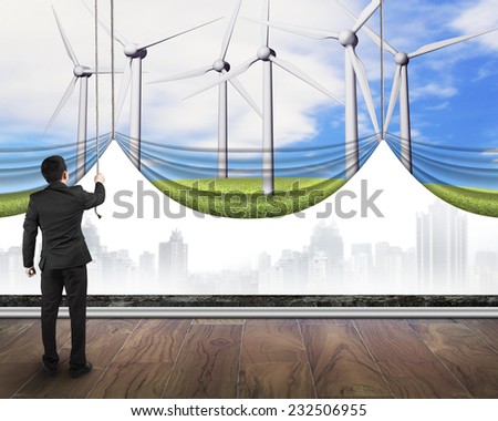 businessman pulling open group of wind turbines curtain covered gray cityscape, environmental protection and alternative energy concept