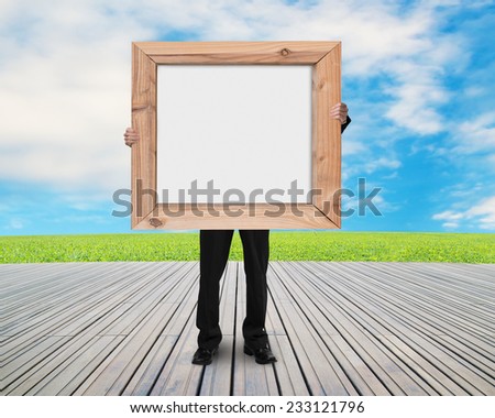 man holding blank white board with wooden frame on wood floor and natural sky clouds grass background