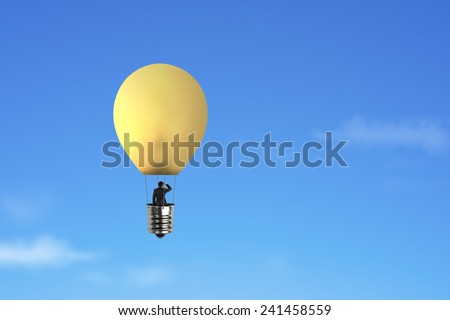 Businessman in brightly yellow lamp hot air balloon flying over blue sky