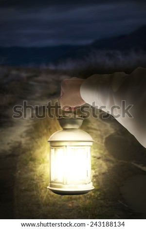 Right hand holding light illuminating dark road at night background