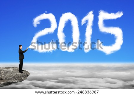 Businessman spraying white 2015 year cloud shape in blue sky cloudscape background