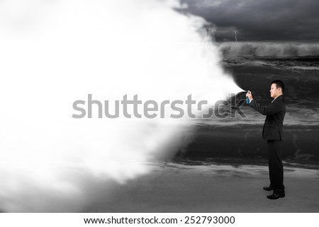 Business man spraying white cloud paint covered dark stormy ocean background
