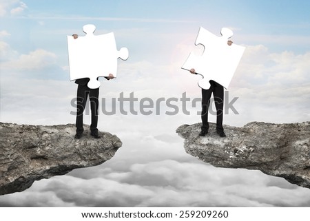 Businessmen holding two white jigsaw puzzles to connect on the cliff with cloudscape sunlight background