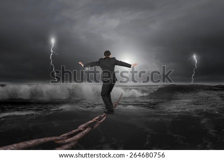 Businessman balancing on old iron chain with dark stormy ocean background