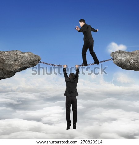 Businessman walking on the broken rusty iron chains another man holding connect two cliffs with sky cloudscape background, business teamwork concept.