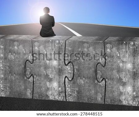 Business man sitting on four huge concrete puzzles connected together, on sky sunlight asphalt road background