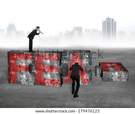 Boss using speaker yelling at employee pushing big jigsaw puzzle concrete blocks with red FEAR word, on concrete floor cityscape skyline background