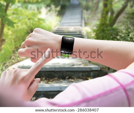 Sport woman finger pointing smart watch with blank black glass bent touchscreen, on forest trail background