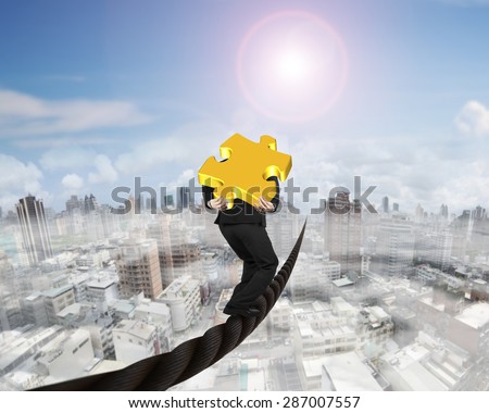Businessman carrying 3D gold puzzle piece balancing on a wire, with sky sun mist cityscape background.